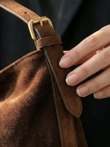 Hand on the strap and brass buckle of The Houle Petite Suede in Chocolate