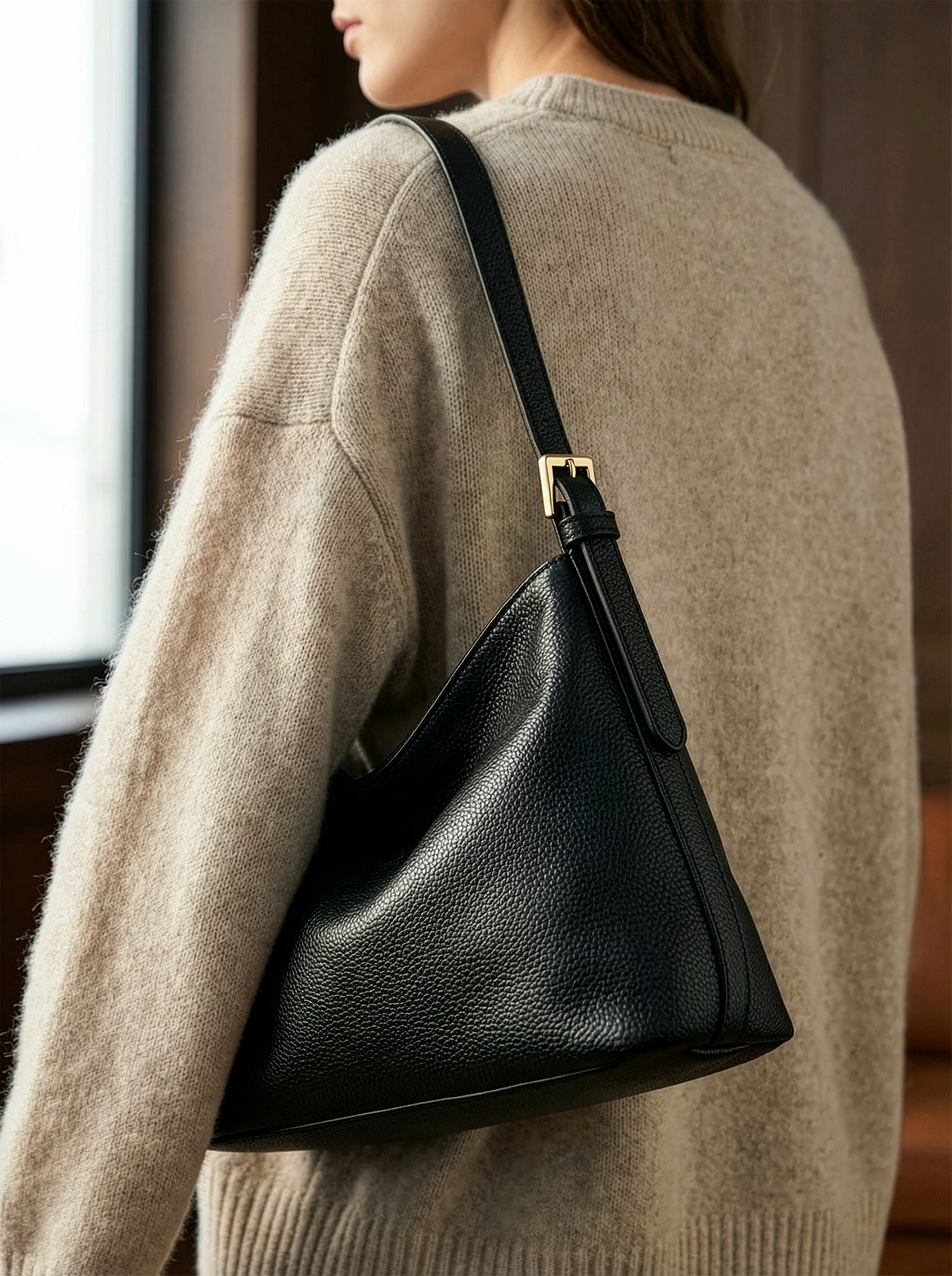 Woman in a beige knit sweater carrying The Houle Petite in Noir on her shoulder