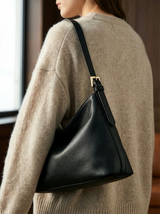 Woman in a beige knit sweater carrying The Houle Petite in Noir on her shoulder