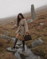 The Aurore Suede Satchel in Espresso, carried by hand in the misty hills